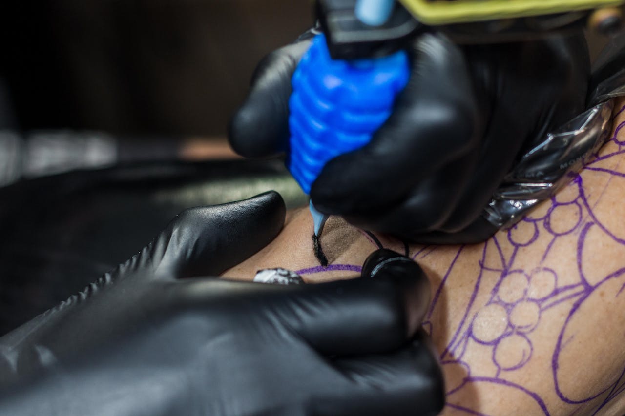 Detailed view of a tattoo artist working on a client's skin using a tattoo machine.